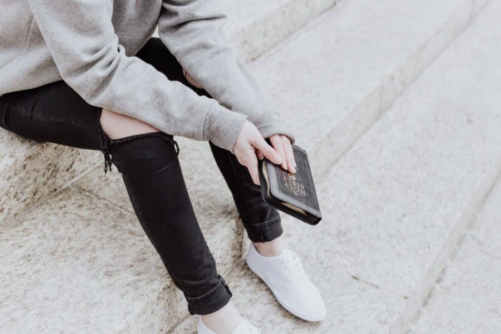 New to the Bible: A woman sitting on stairs with a Bible in her hand